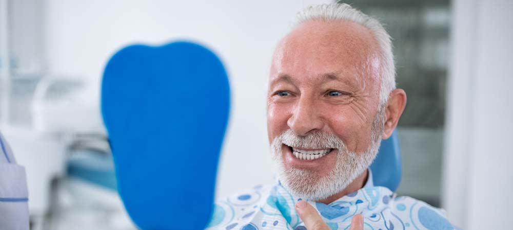 Man smiling in mirror with new dentures